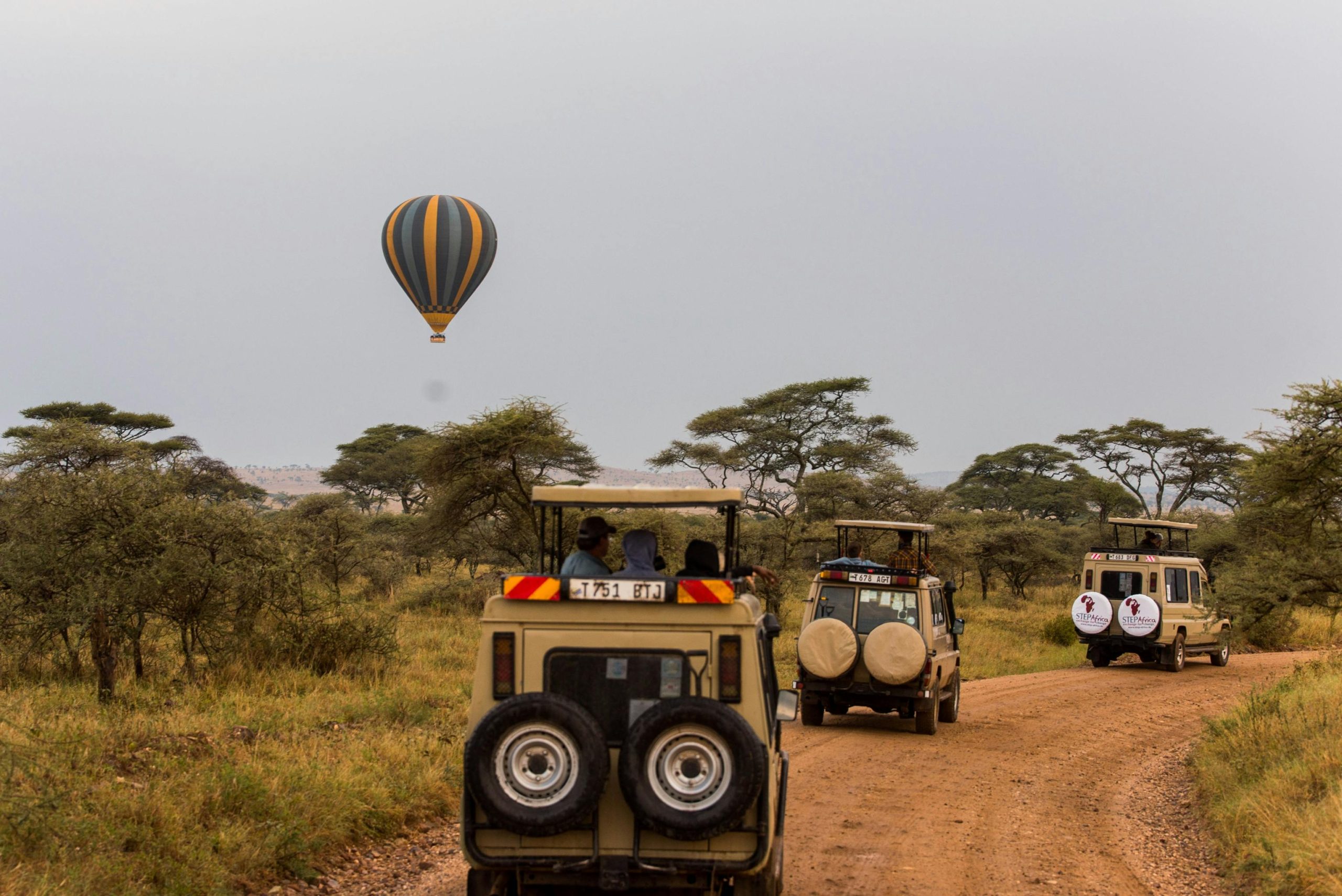 Tourists in tour land cruisers and a hot air balloon at a distance